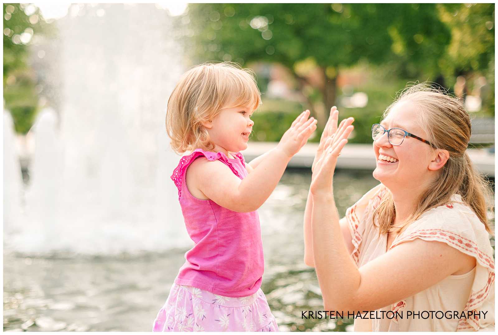 Mom and toddler daughter playing pat-a-cake in front of a fountain. Cantigny Park photography by Kristen Hazelton