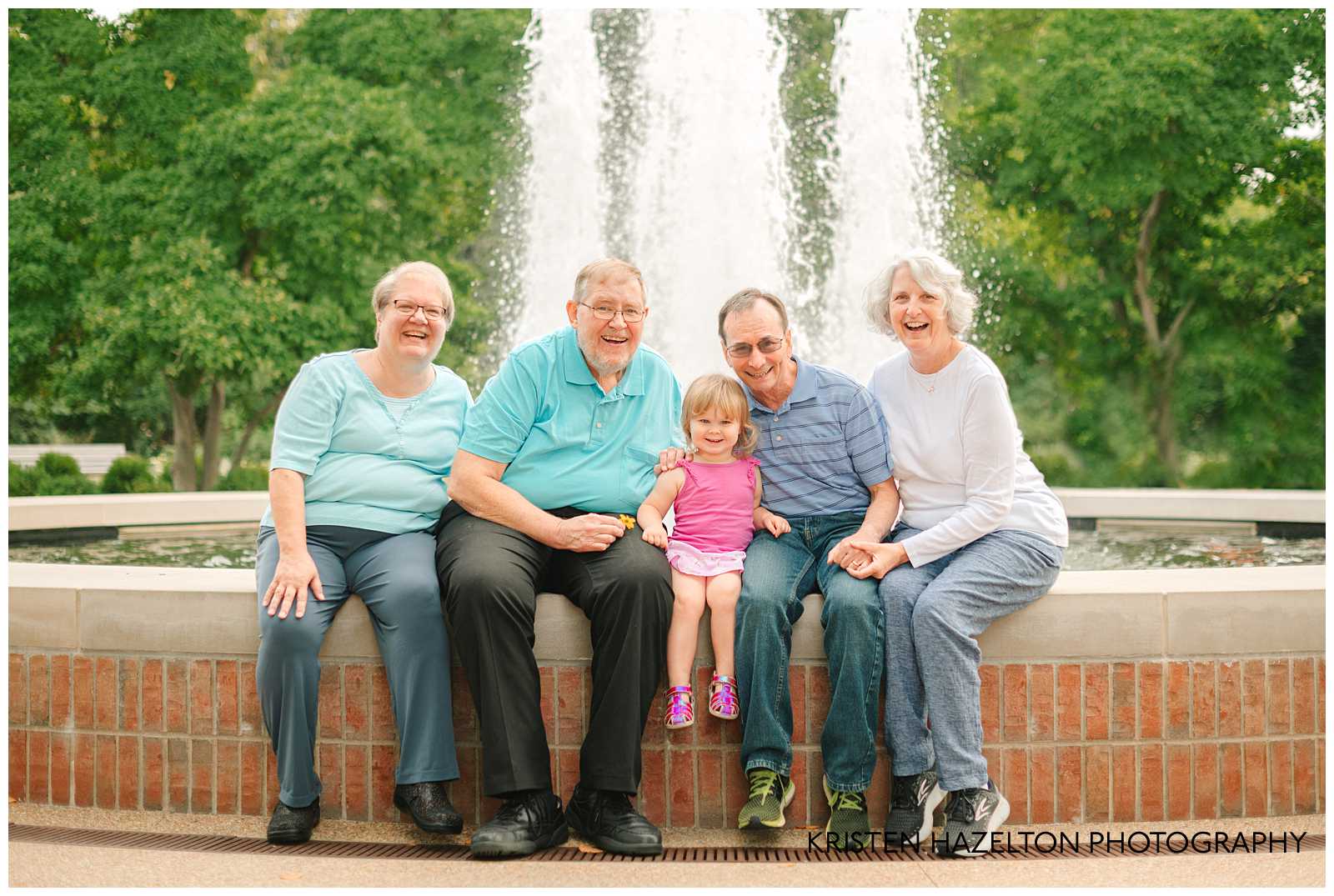 Toddler girl and two sets of grandparents sitting next to a fountain. Cantigny Park photography by Kristen Hazelton