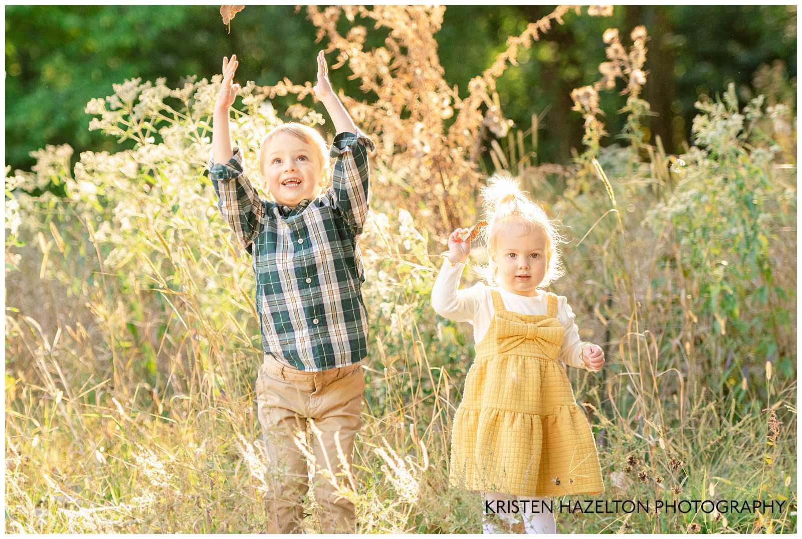 Toddler brother and sister throwing leaves in a field of yellow grass and wildflowers
