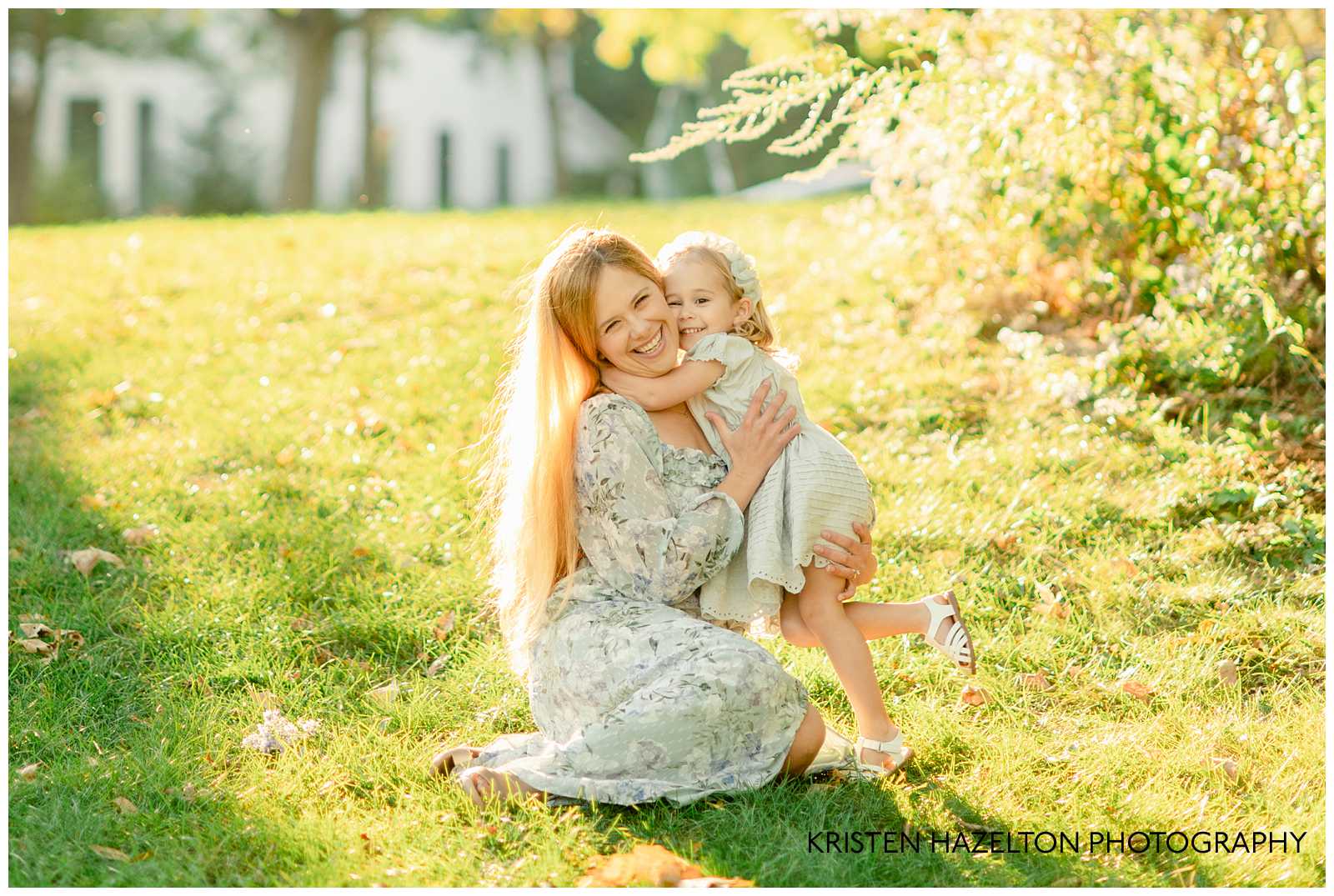 Toddler daughter hugging her mom! Both are wearing light blue dresses and standing on grassy hill