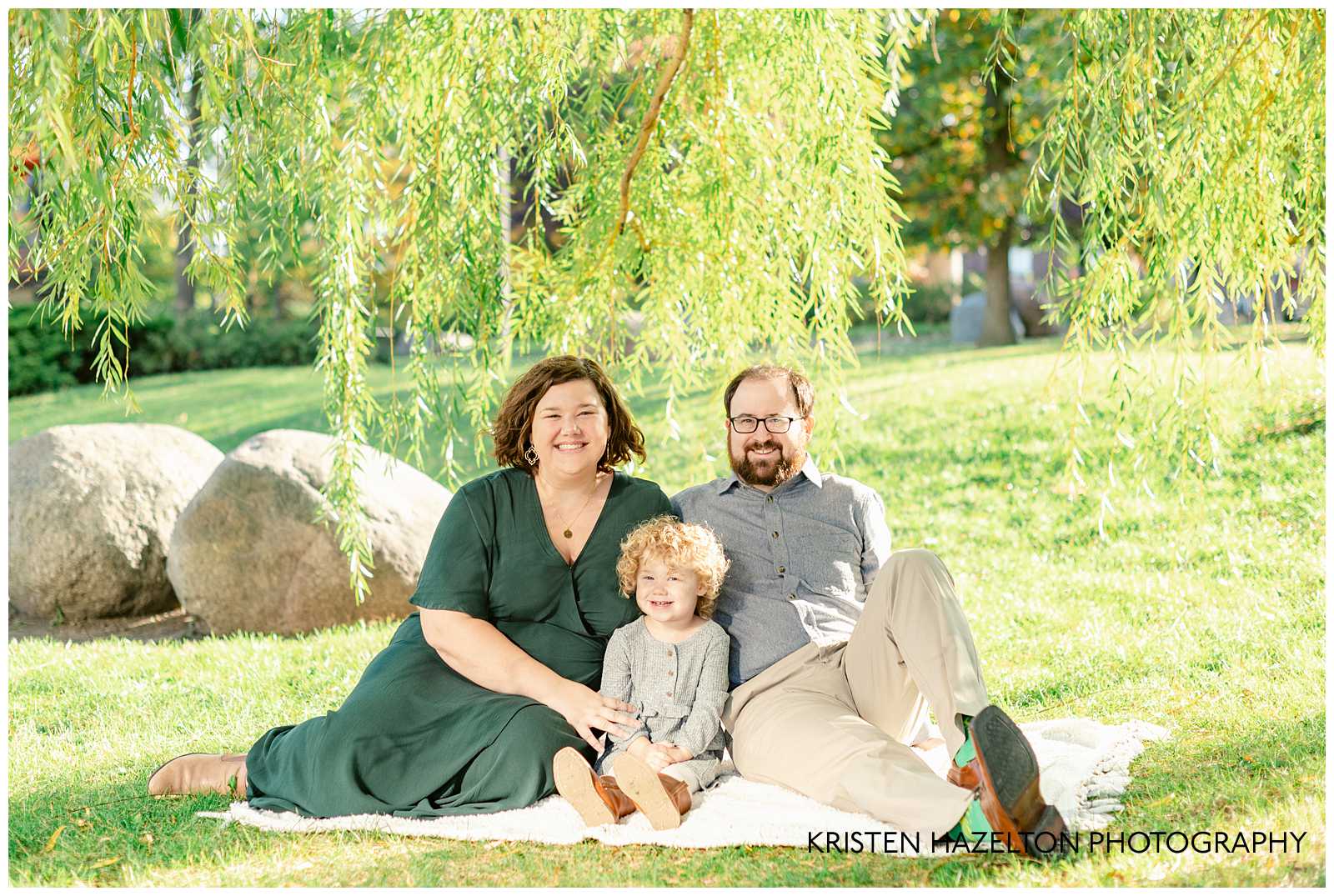 Mom, Dad, and young daughter on a white blanket under a willow tree
