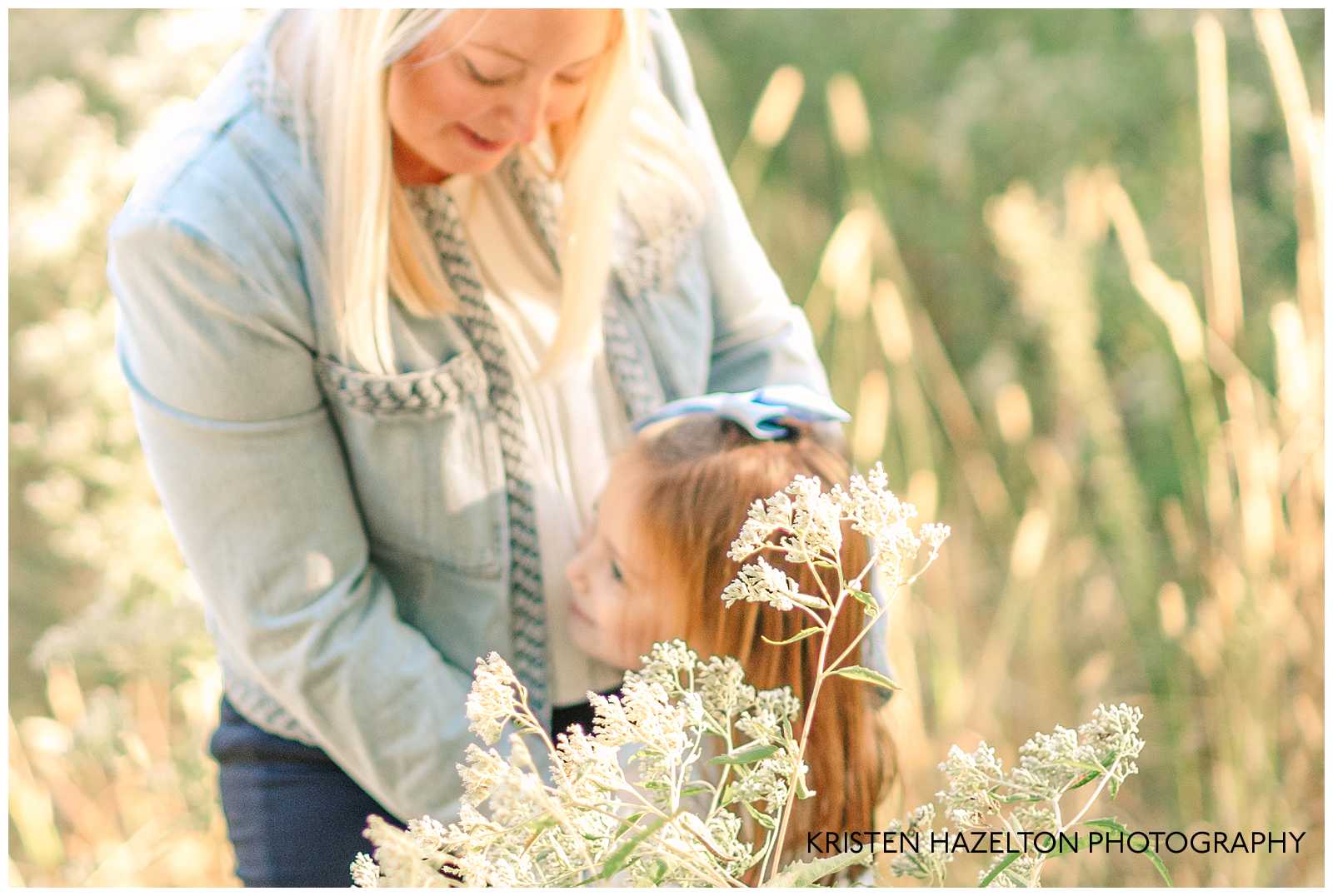 Out of focus shot of a mom looking down and hugging her young daughter in a field of flowers