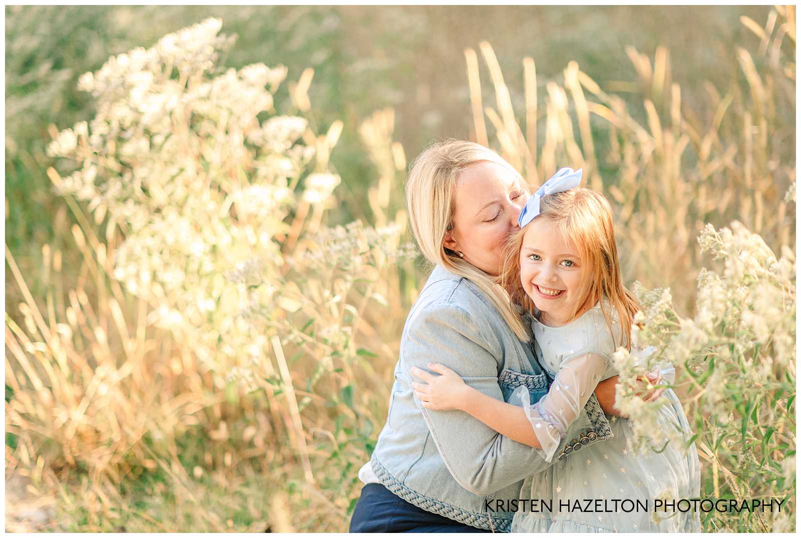 Mom crouching down and kissing her daughter's cheek in a field of wildflowers and grass. River Forest IL family portraits by Kristen Hazelton