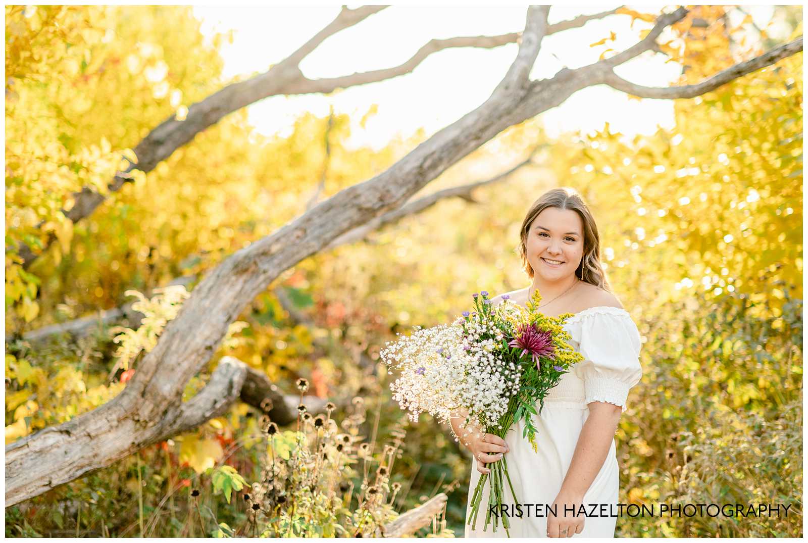 High school senior girl wearing a white dress and holding a bouquet of wildflowers