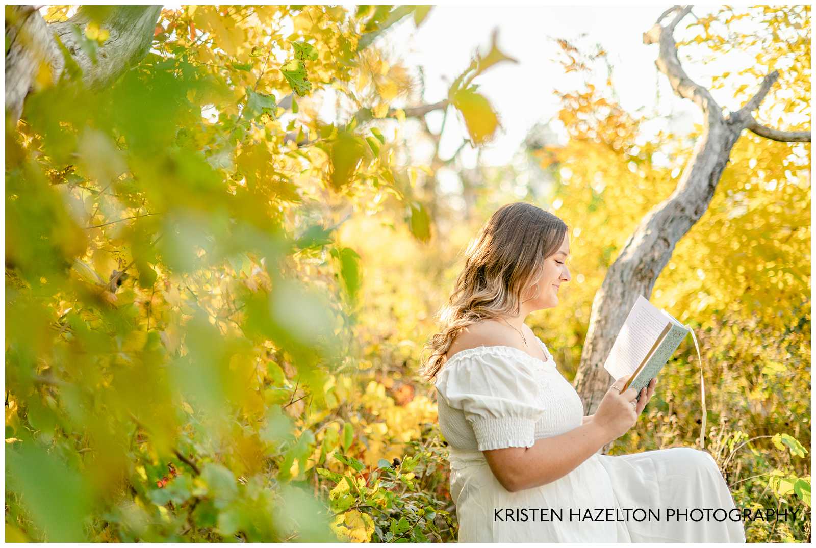Cottagecore photoshoot of a girl in a white dress reading a book while sitting in a tree