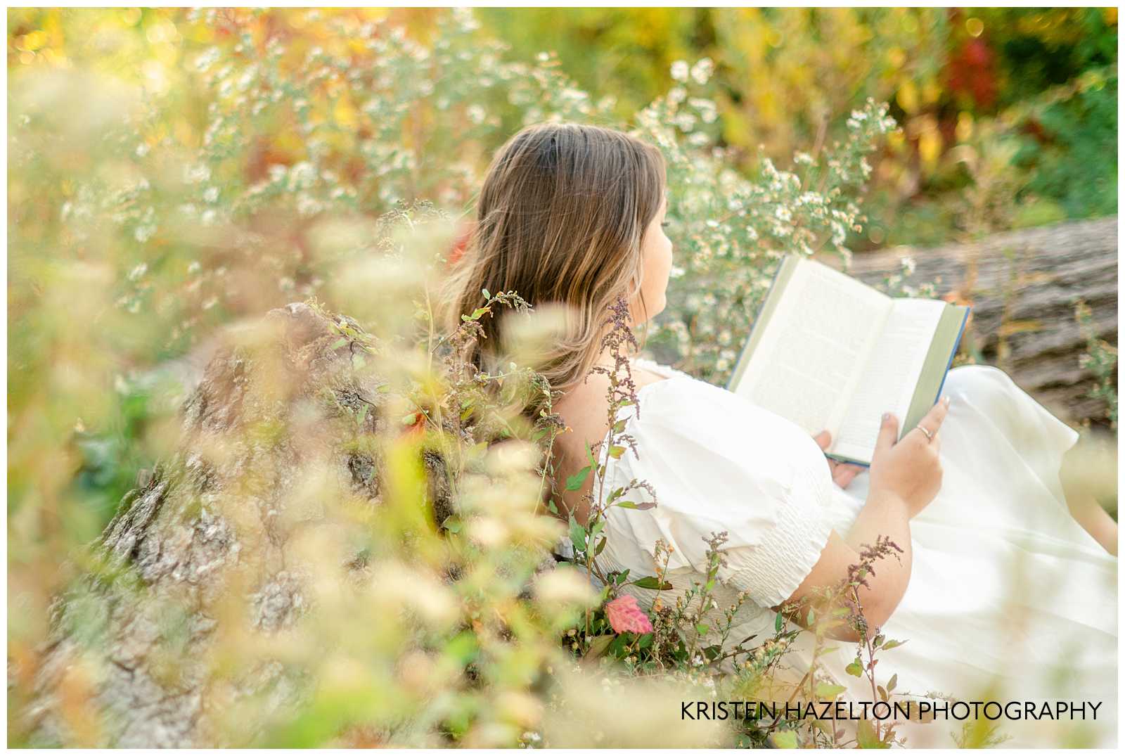 Books aesthetic photoshoot in Chicago; high school senior girl wearing a white dress reading a book while leaning against a tree stump