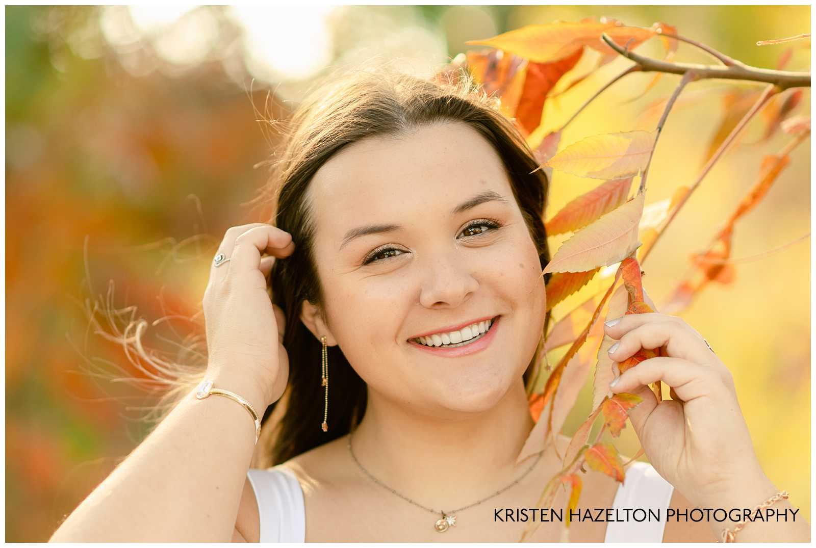 Senior girl holding her hair back next to a tree with orange leaves