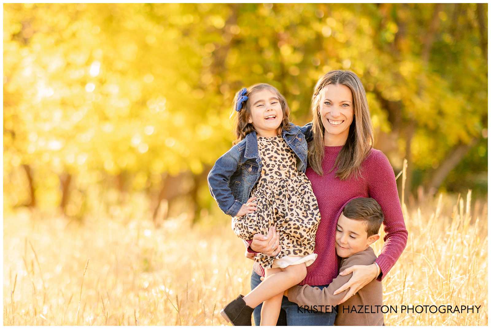 Mom laughing with her kids in a field of yellow grass with bright yellow leaves behind them during their fall family photos in River Forest, IL.