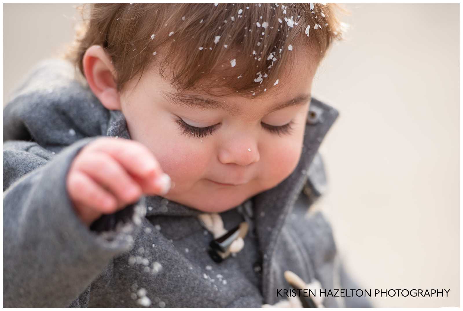 Toddler boy playing in the snow with snowflakes in his eyelashes, hair, and on his nose
