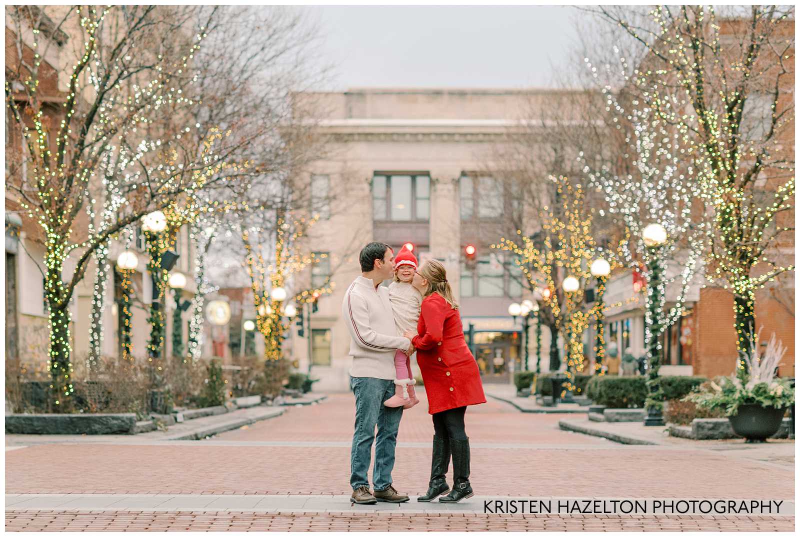 Mom and Dad kissing their toddler daughter on the cheek for their holiday family photos in downtown Oak Park on Marion Street