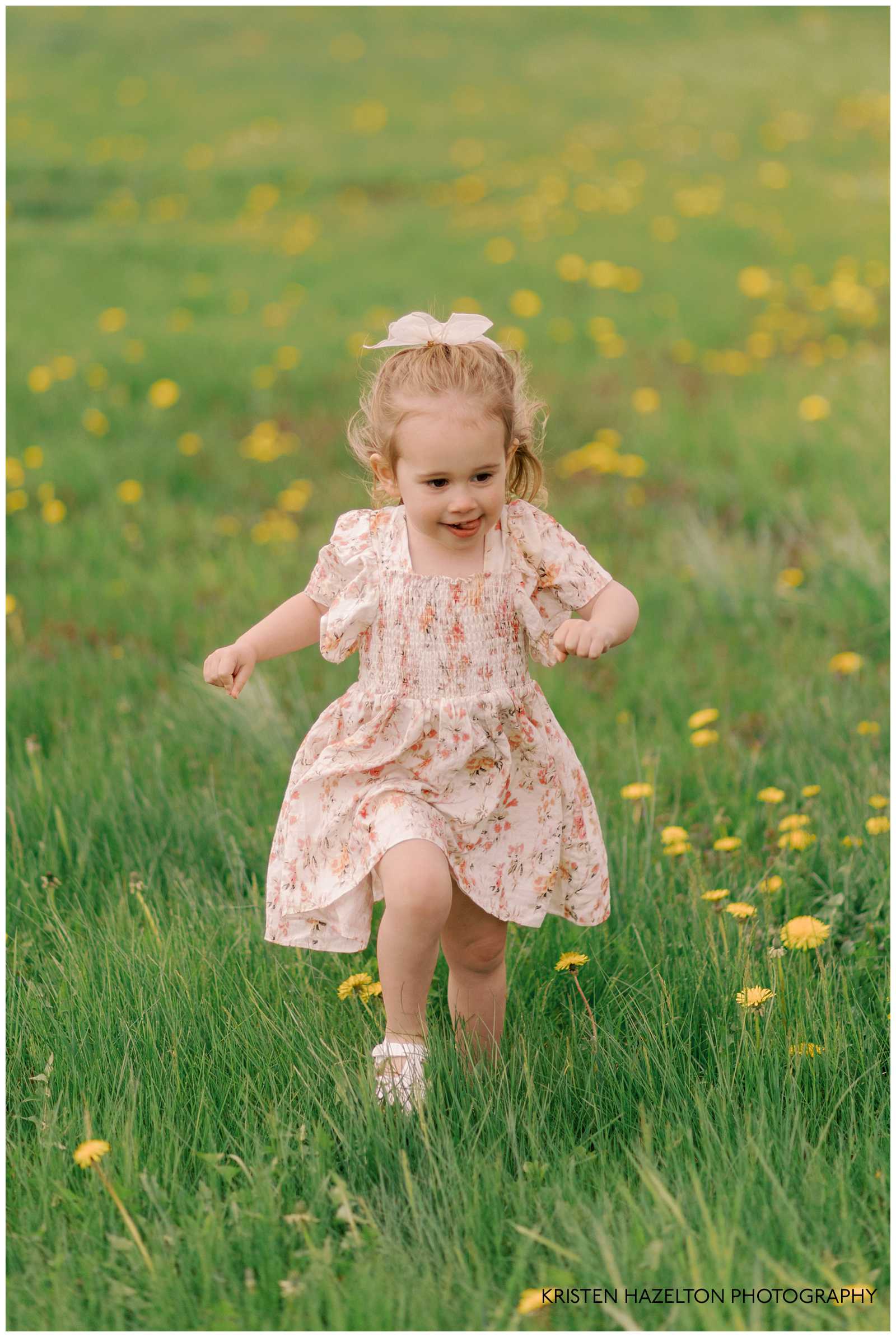 Little girl in pink floral dress running across a green field with yellow dandelions