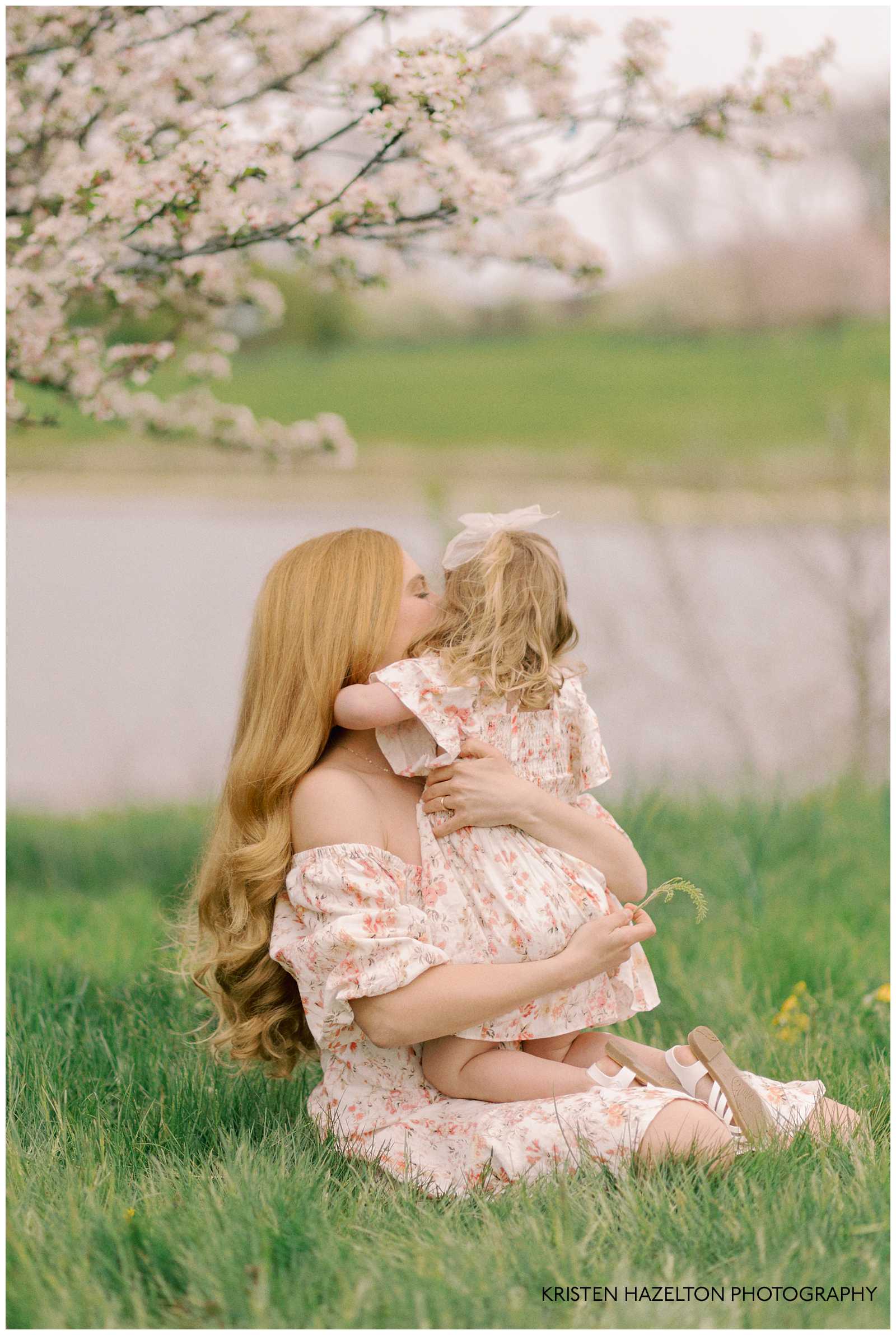 Mother hugging young daughter under a tree with white flowers. Both are wearing pink floral dresses for their St Patrick's Day in Chicago photoshoot