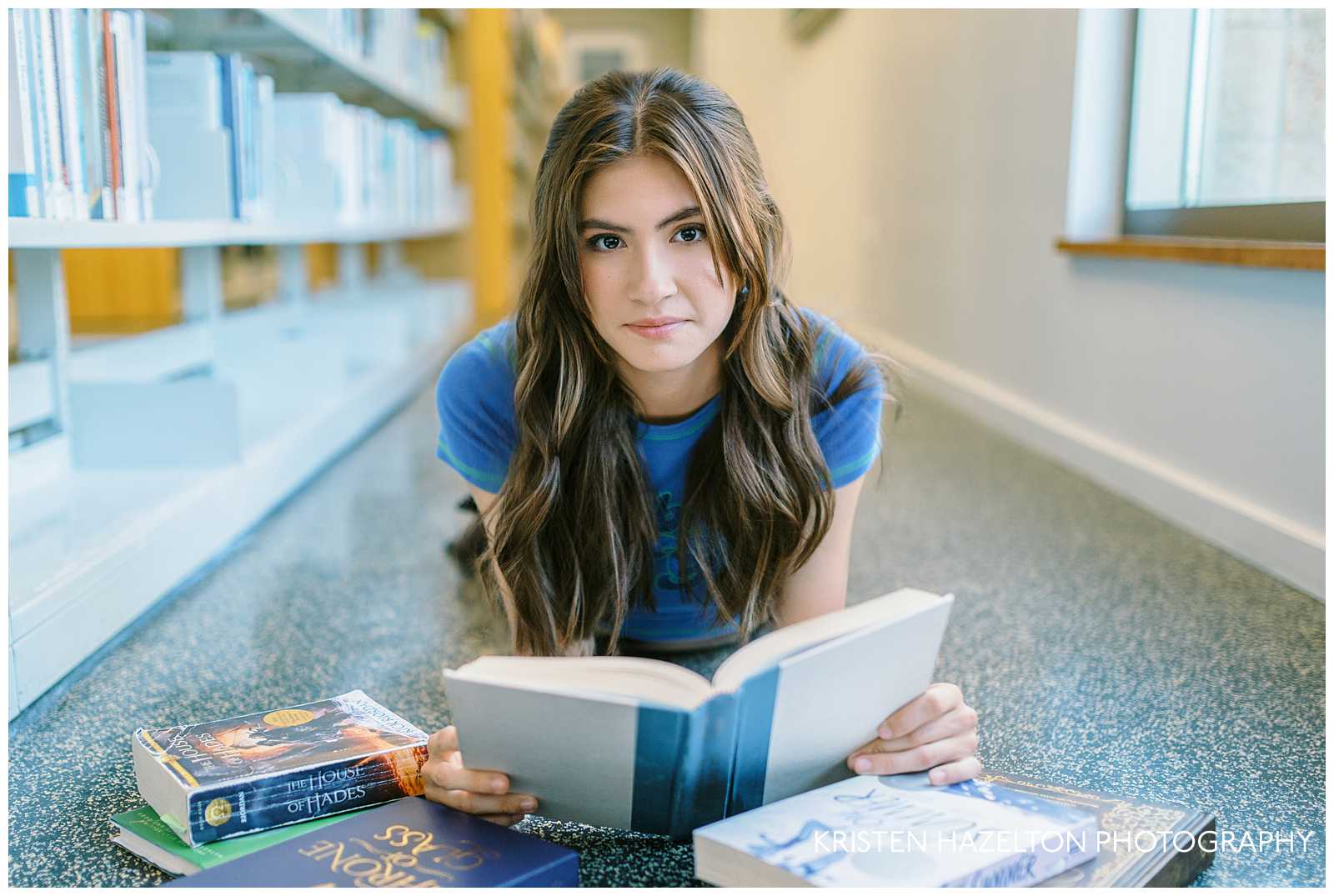 Girl with brown hair and a blue tee shirt lying on the floor of the library for her library senior pictures.