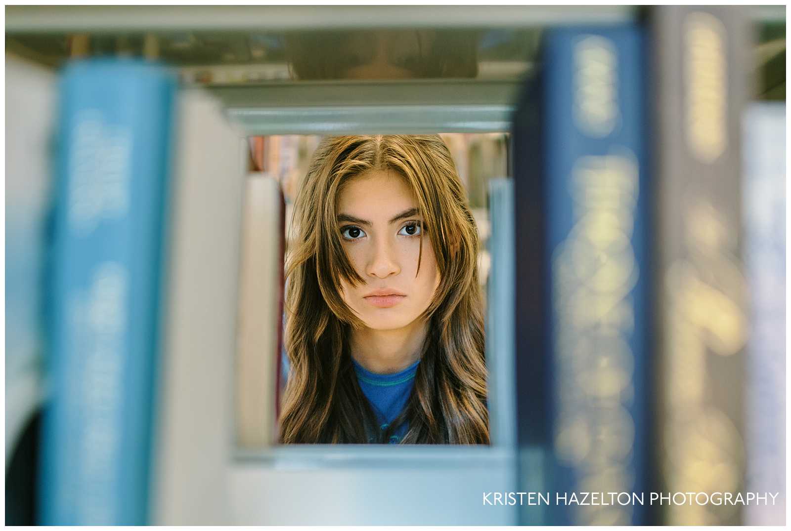 Library photo ideas: a girl looking through two shelves of books and framed by books. 