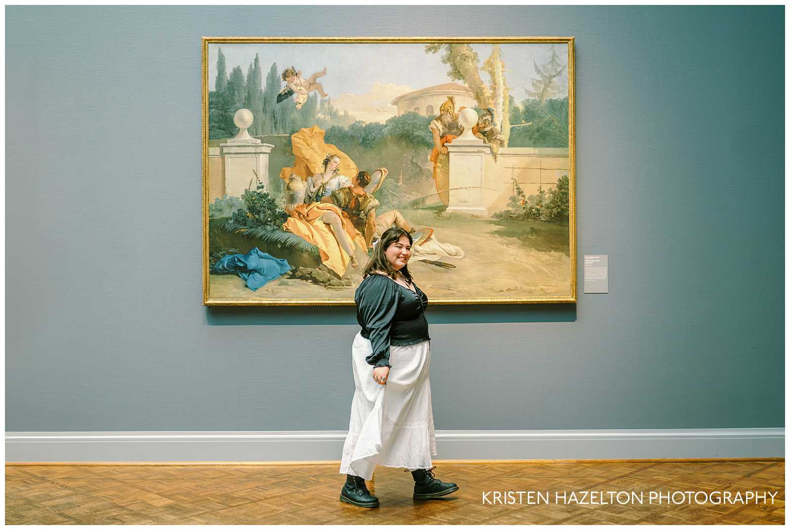 Girl wearing a black blouse and white skirt walking in front of a painting for her photoshoot in a museum by Chicago Photographer Kristen Hazelton