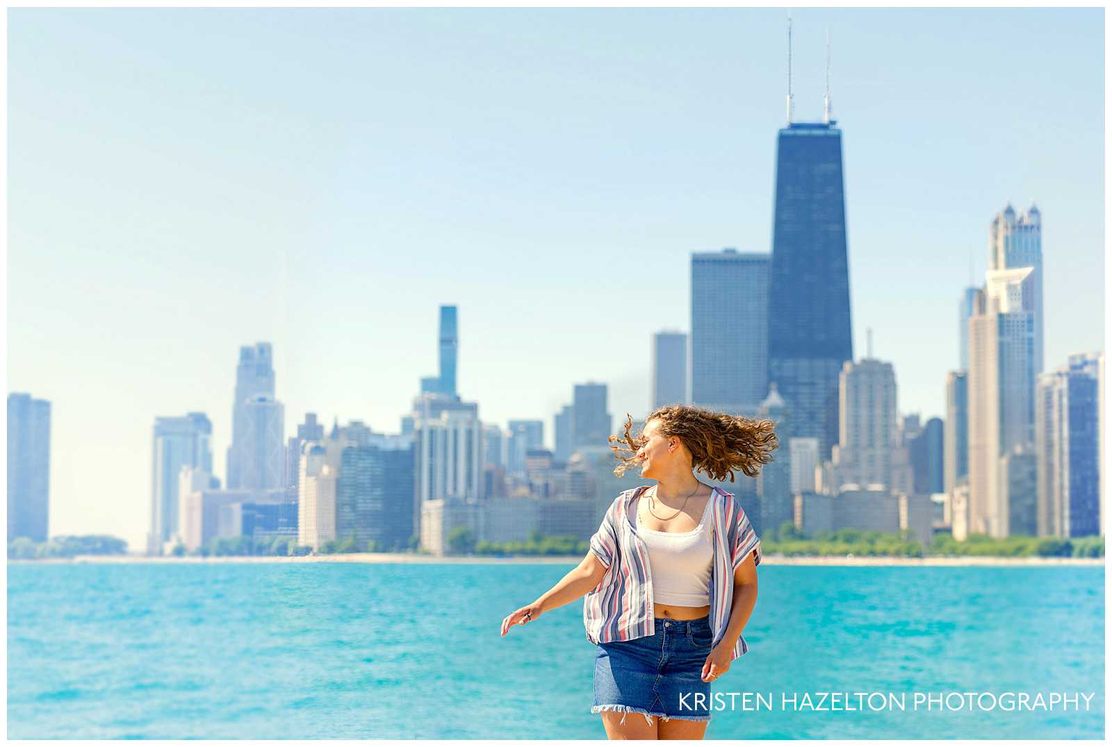 High school senior girl with brown curly hair dancing in front of the Chicago skyline at North Avenue Beach for her beach senior pics