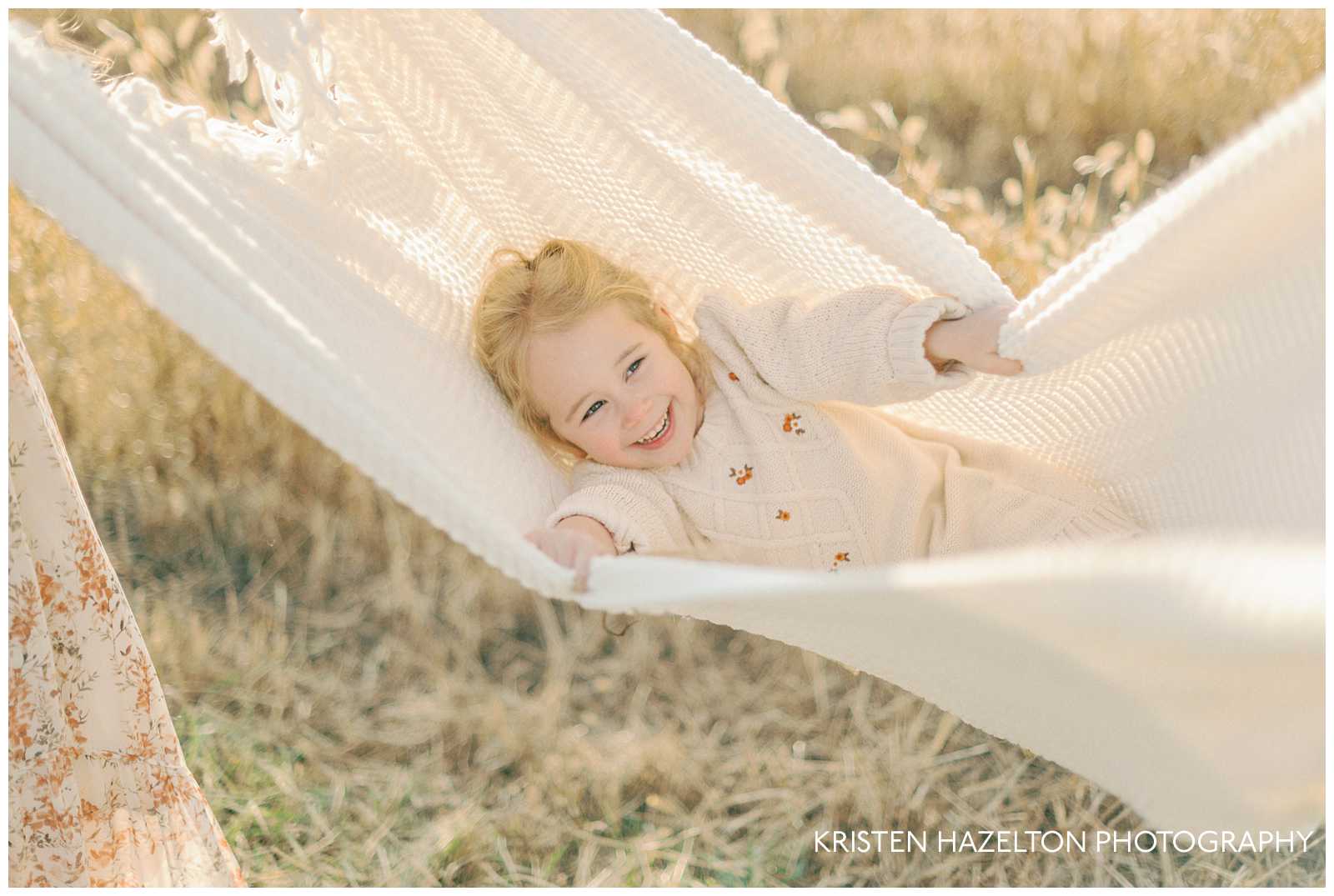 Little girl wearing a white sweater dress being swung in a blanket by her mom and dad