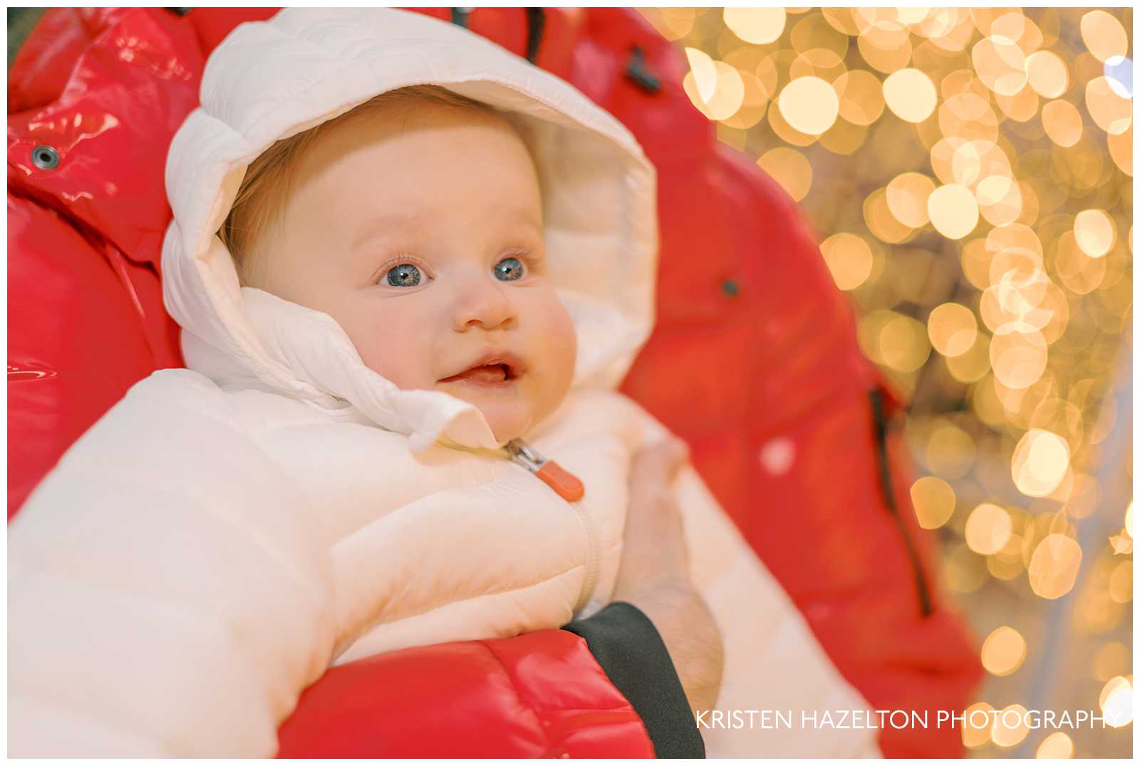 Baby in white snowsuit smiling as he looks at Christmas lights for the first time at the Jack Frost holiday pop up in downtown Chicago