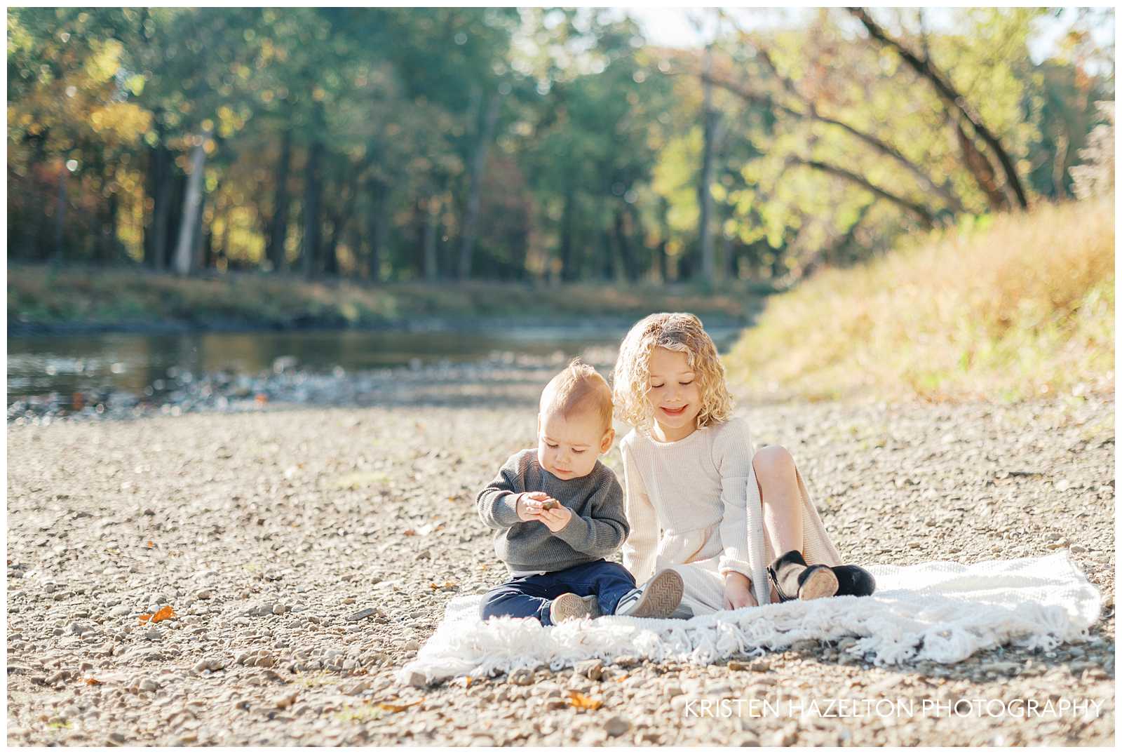 Little girl in white dress seated on a blanket next to her brother and the Salt Creek in Fullersburg Woods