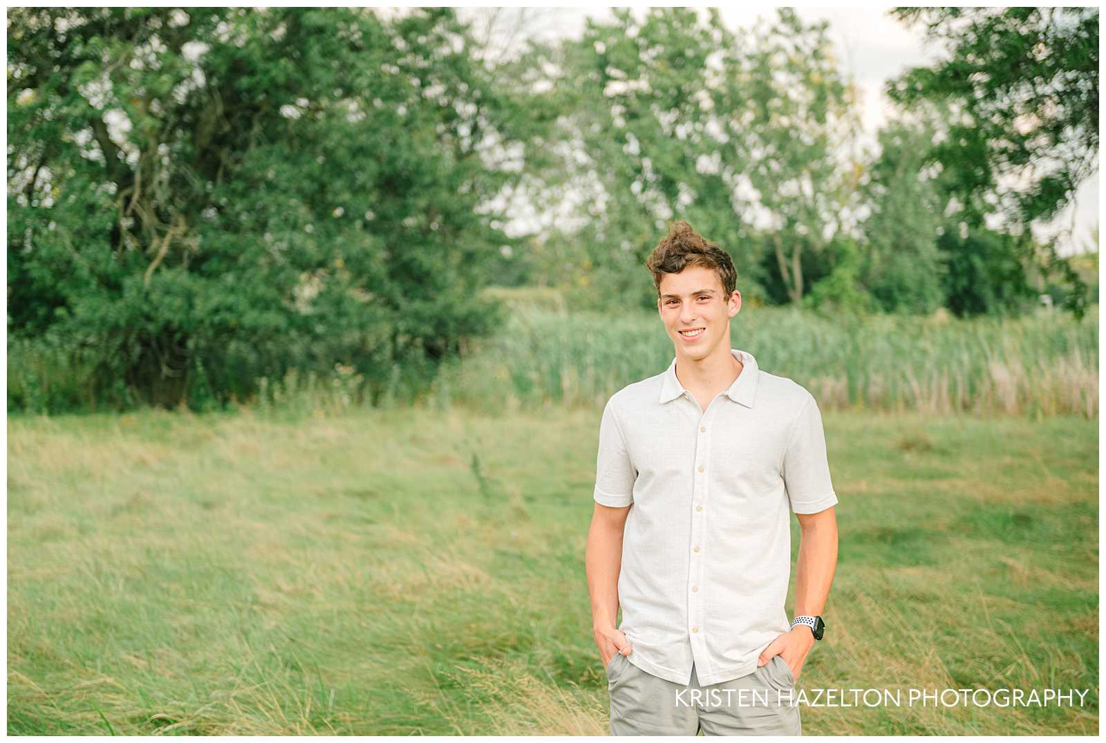 High school senior guy wearing a white shirt and standing in a field with his hands in his pockets