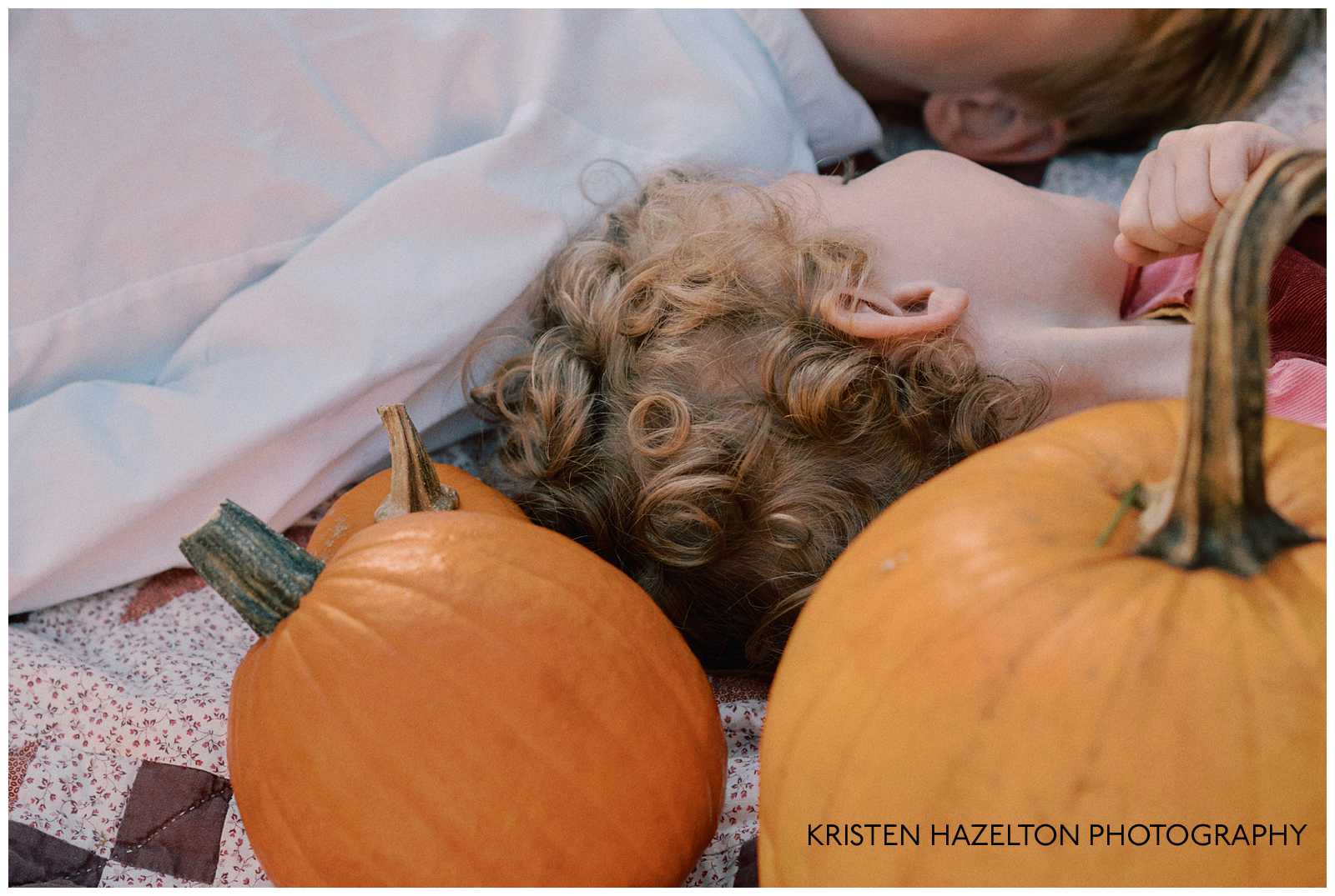 Little girl with curly hair lying on a quilt with pumpkins