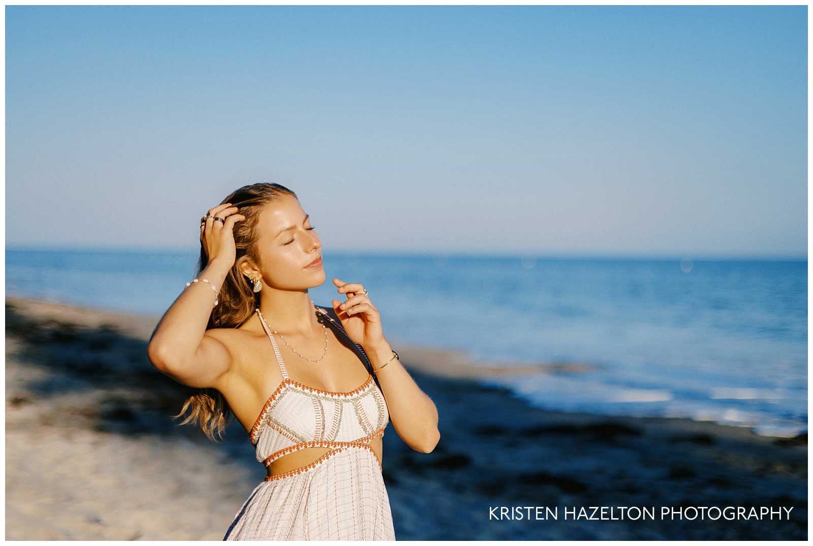 Santa Barbara graduation portraits at Butterfly Beach Montecito; a girl in a white dress closing her eyes and looking towards the sun