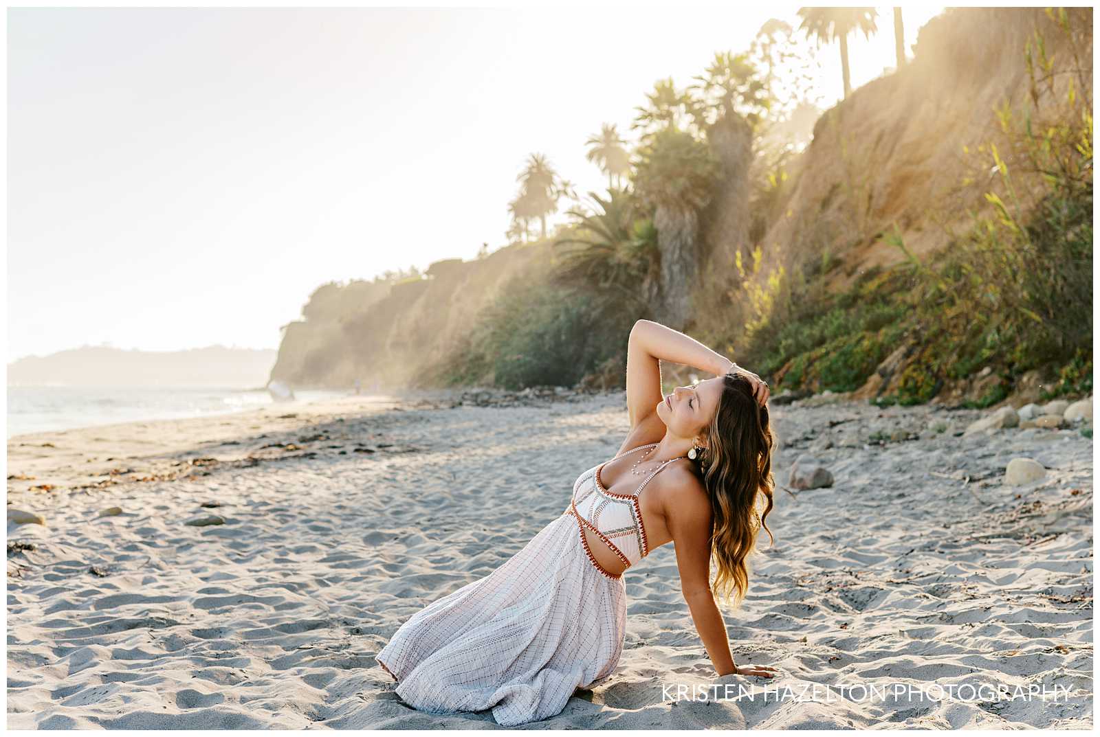 Butterfly Beach pictures - a girl in a white dress sits in the sand and looks toward the ocean