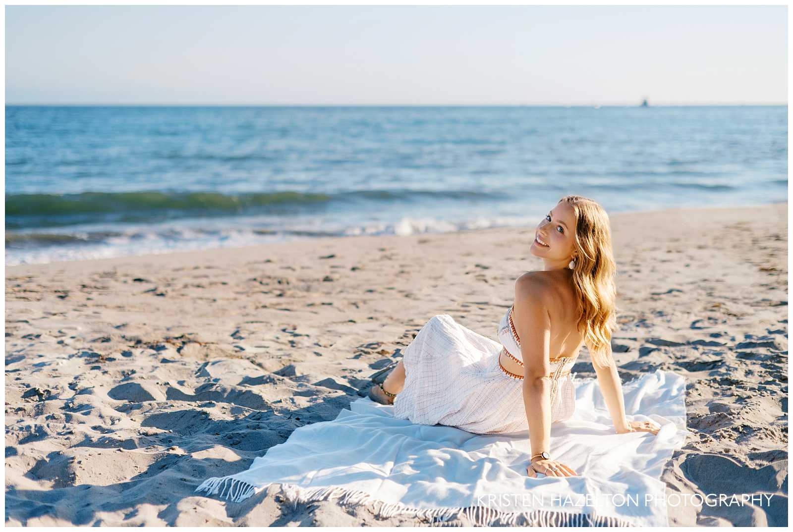 Girl in white dress sitting on a white blanket for her beach portraits in Montecito, CA