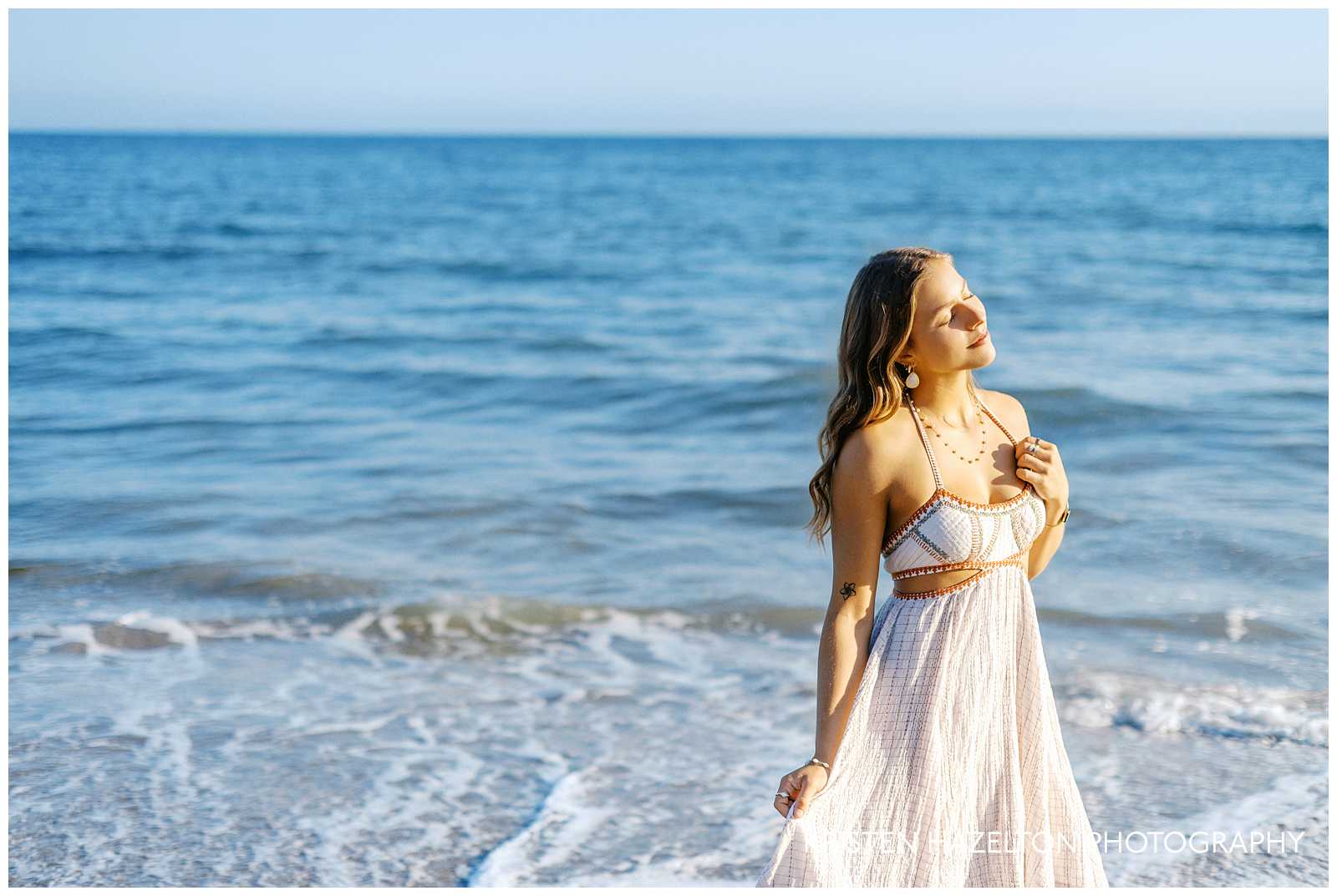 Santa Barbara graduation portraits at Butterfly Beach Montecito; a girl in a white dress closing her eyes and looking towards the sun