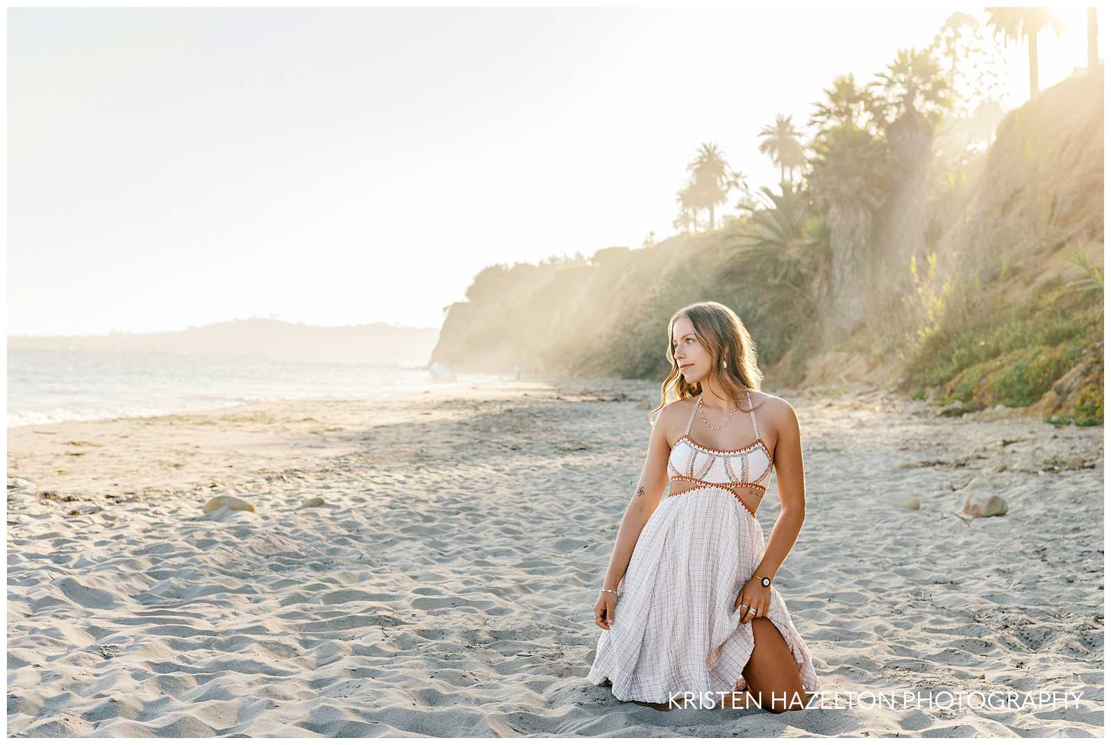 Butterfly Beach pictures - a girl in a white dress sits in the sand and looks toward the ocean