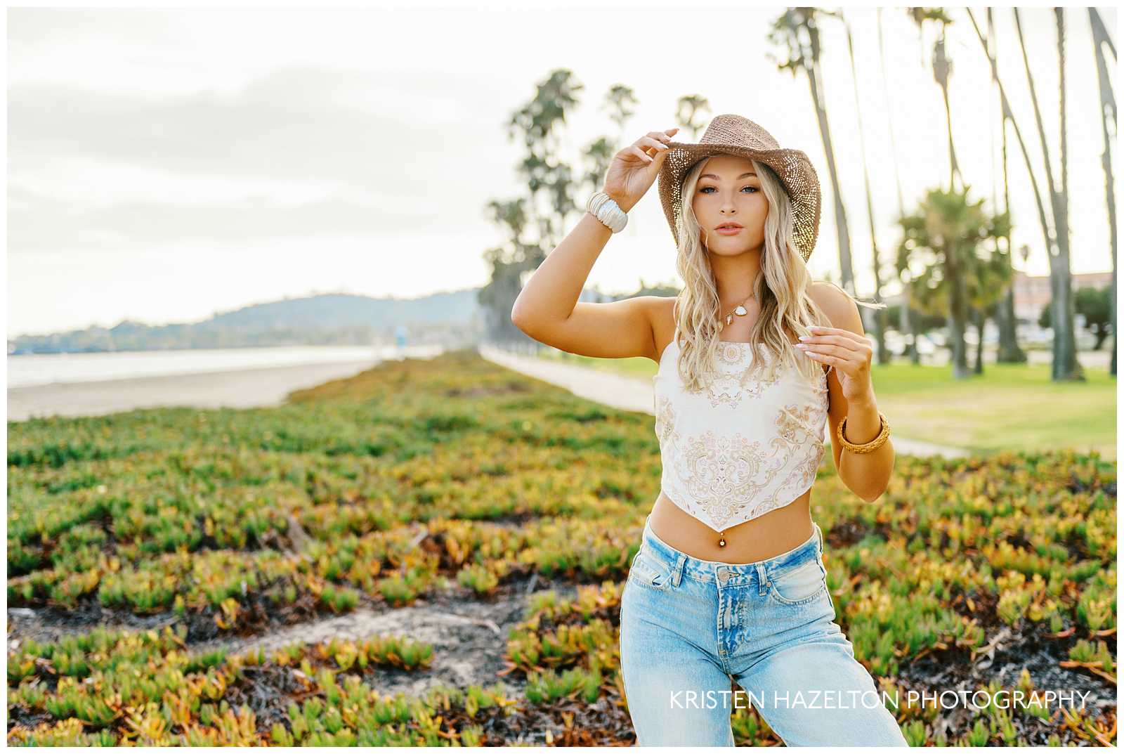 High school senior girl leaning forward while tipping the brim of her hat for her coastal cowgirl photoshoot