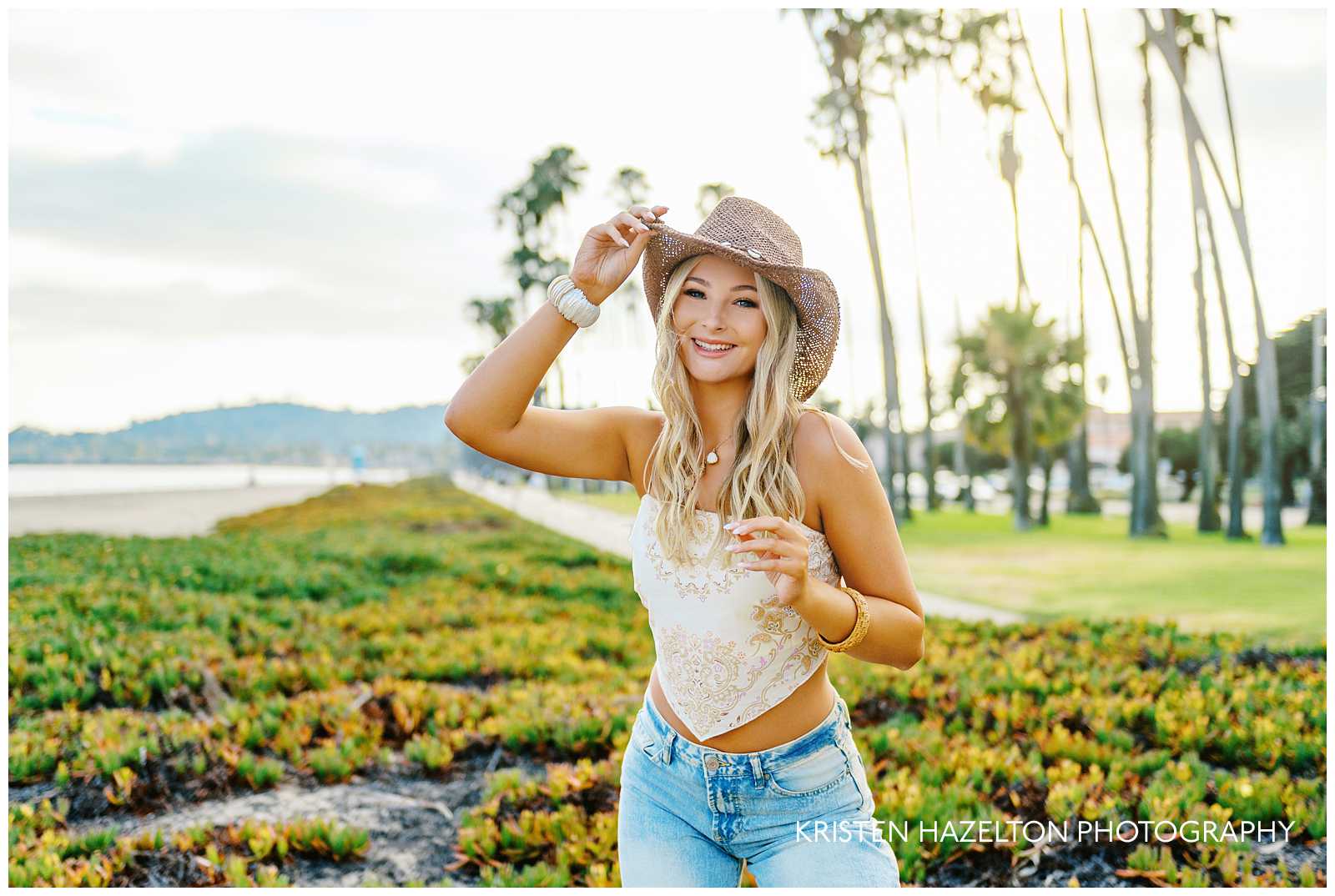 High school senior girl leaning forward while tipping the brim of her hat for her coastal cowgirl photoshoot