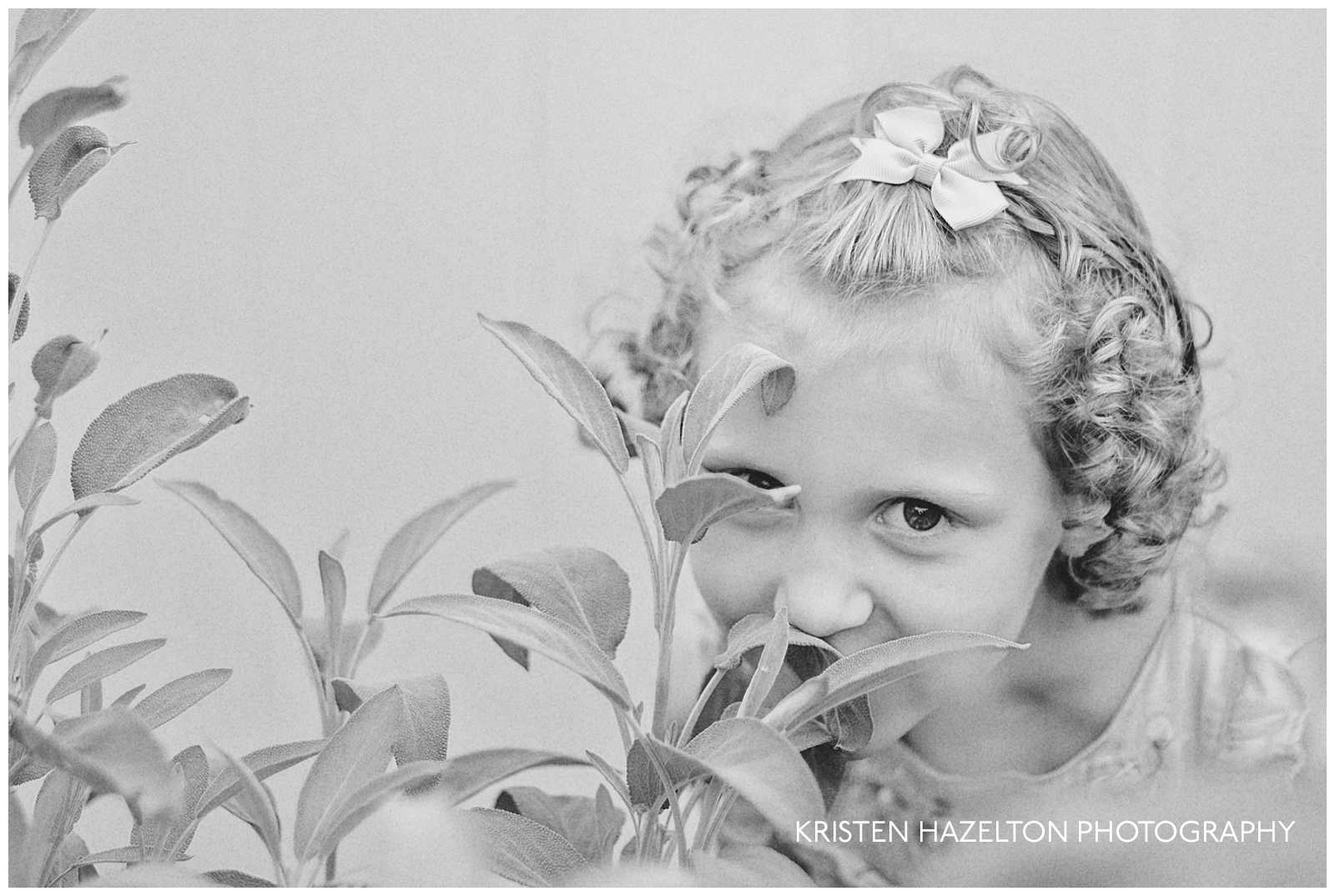 Black and white photo of a girl with curly hair smelling a sage plant