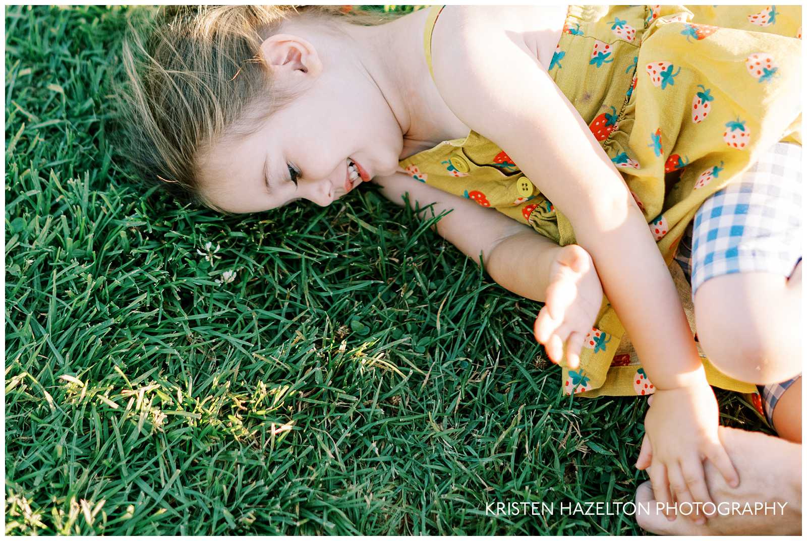 Little girl in a yellow dress rolling on the grass