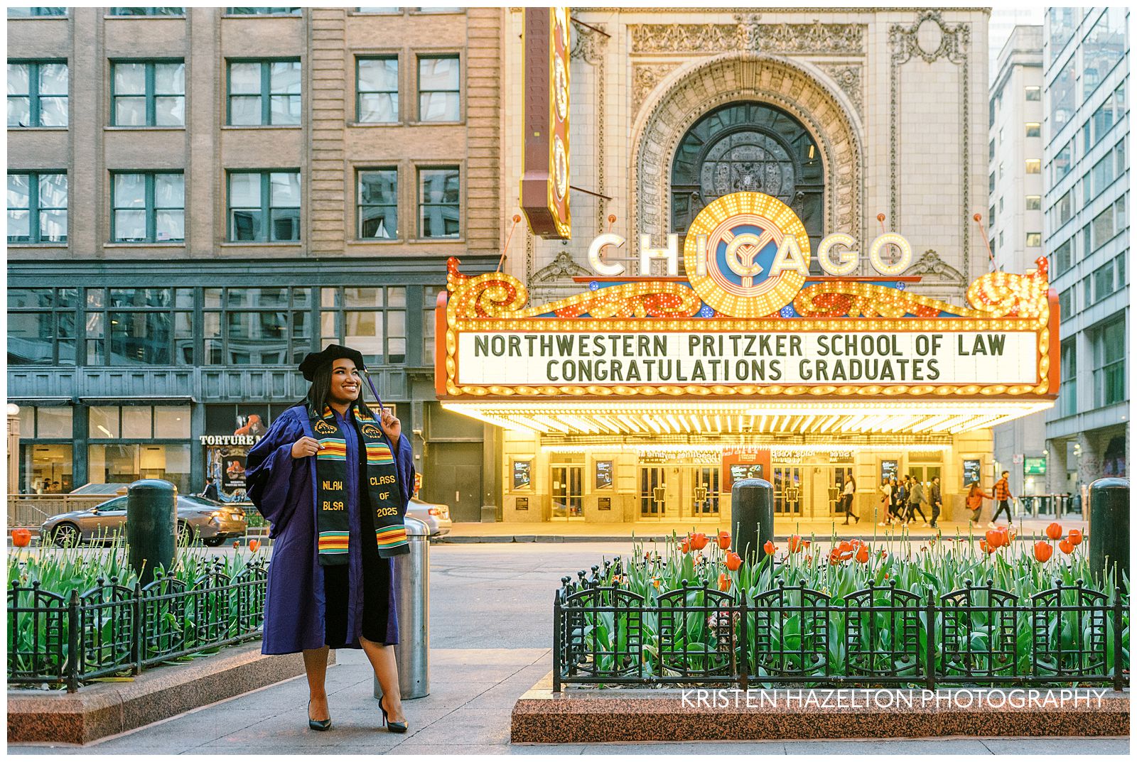 A graduate stands on the sidewalk across the street from the Chicago Theatre