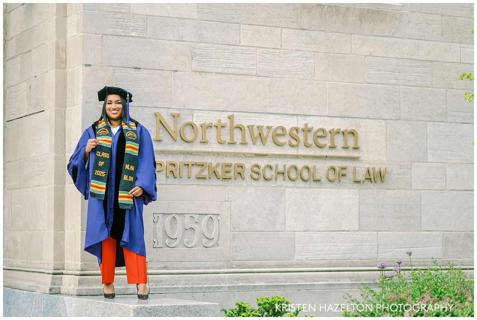 Northwestern graduation portraits at Pritzker School of Law; a graduate in a purple judicial degree robe and red pants stands in front of the logo.