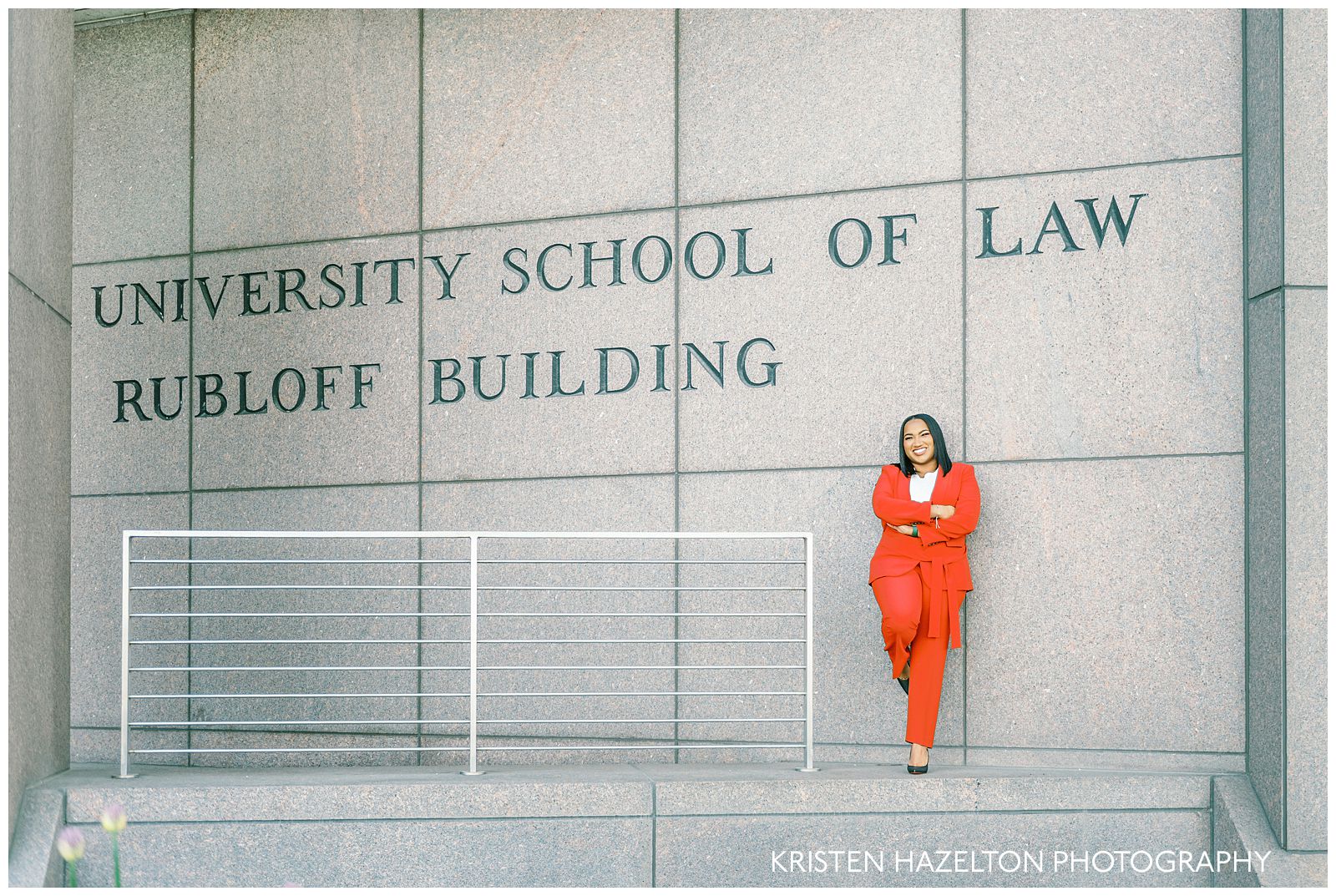 Woman in red suit stands next to the sign for the University School of Law Rubloff Building for her Northwestern graduation photos