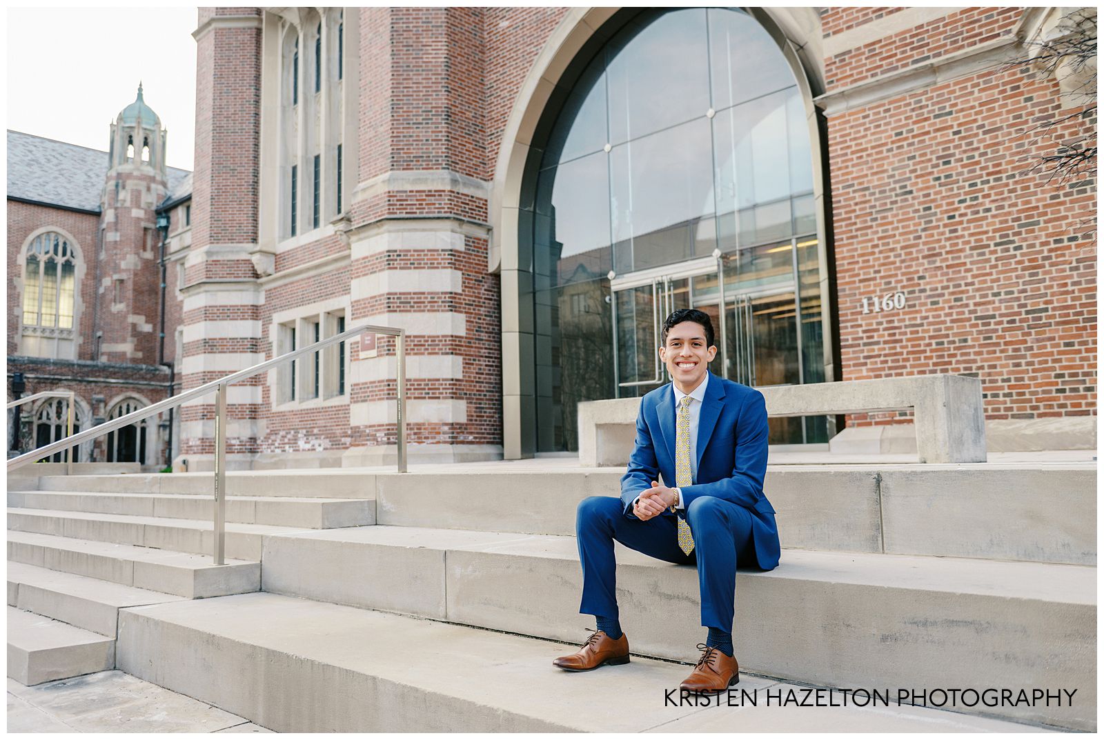Man in blue suit seated in front of a university building