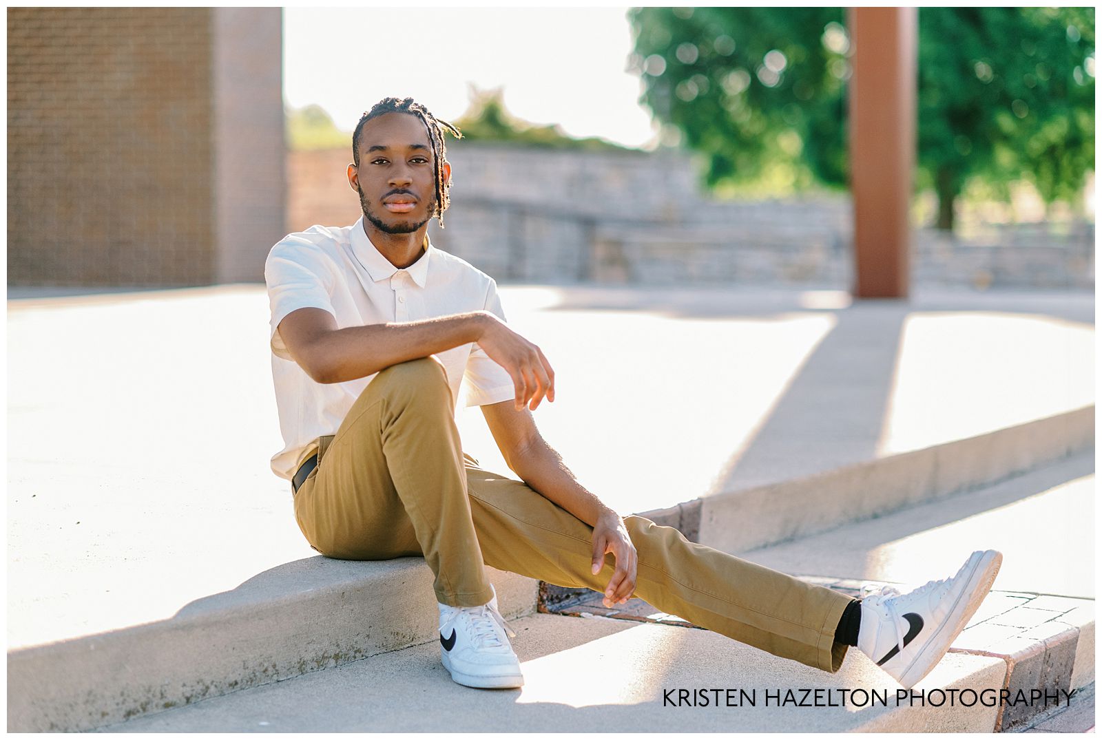 Male high school senior with locs sitting on the steps of an amphitheater for his portraits by northwest Indiana graduation photographer Kristen Hazelton